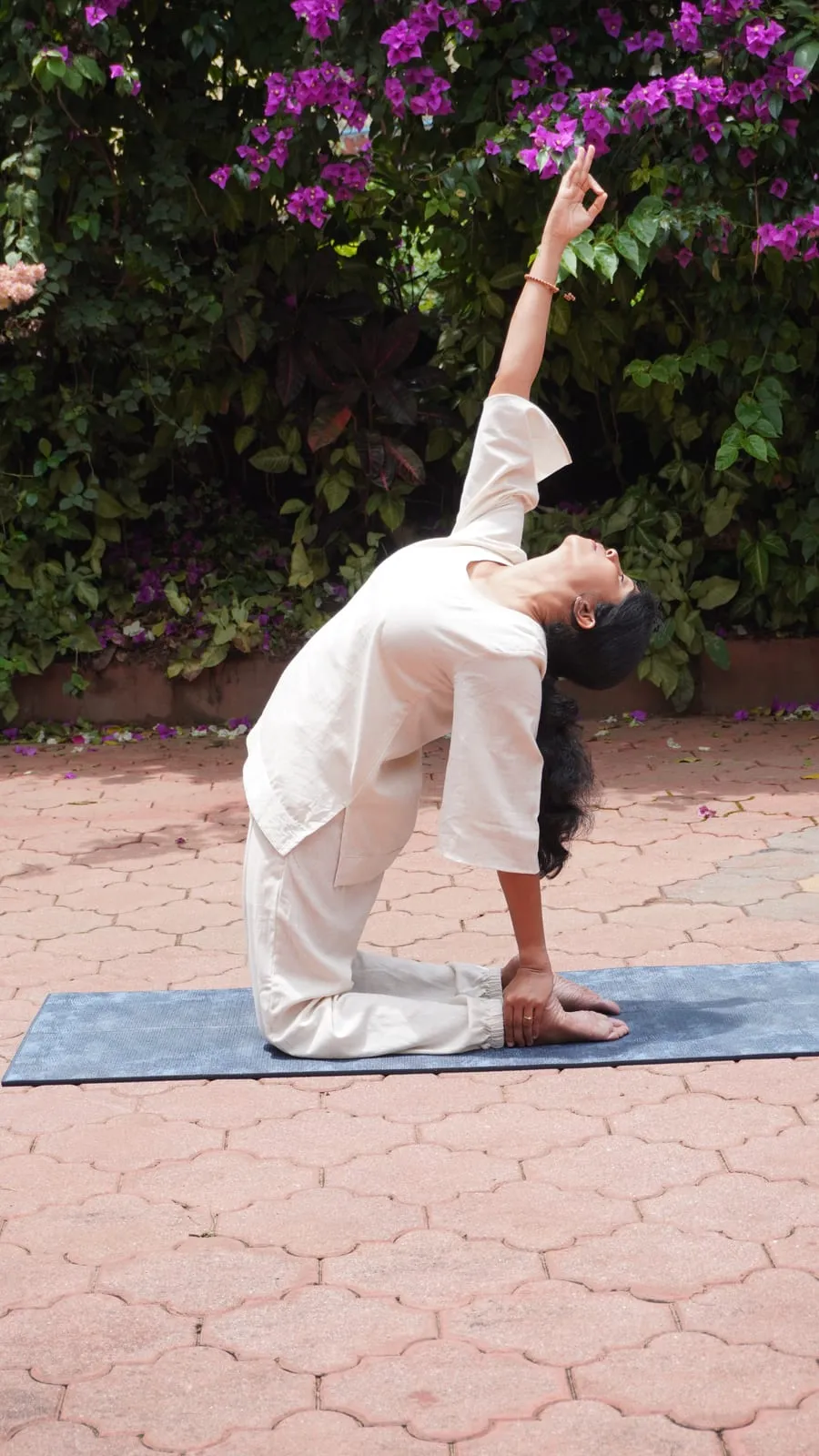 Jagruthi kneeling in a backbend on a mat, one hand reaching back to her heel and the other lifted overhead
