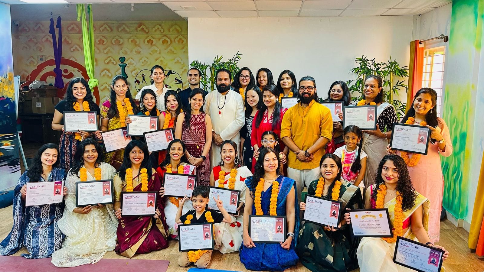 The full teacher training batch and their teachers gathered for a group photo, each holding a framed certificate